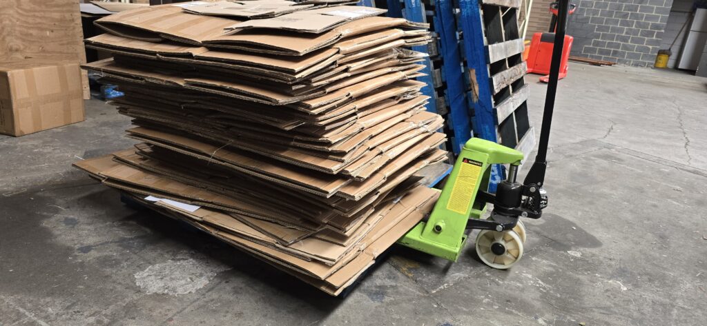 Large stack of flattened cardboard boxes generated at a single packing station in one shift at FulfillWorks warehouse, ready to be reused or recycled