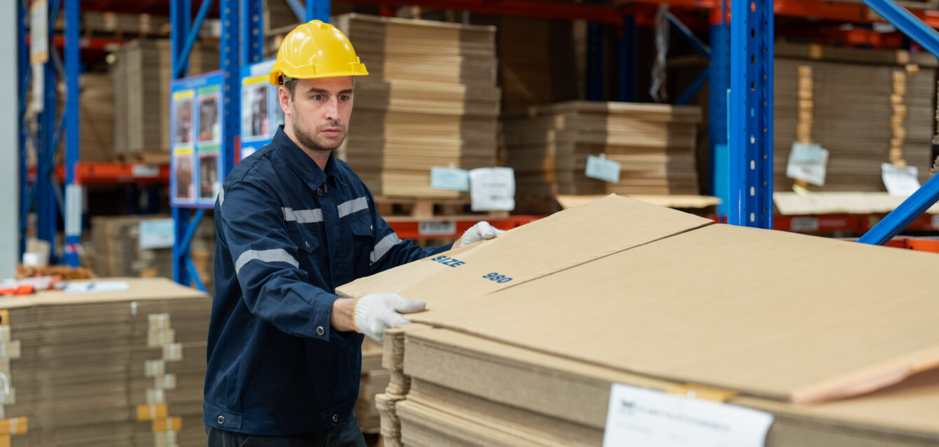 Male warehouse worker preparing cardboard boxes or corrugated paper sheet products for shipping to customer at warehouse store. Logistics, Distribution Center concept Male warehouse worker preparing cardboard boxes or corrugated paper sheet products for shipping to customer at warehouse store. Logistics, Distribution Center concept